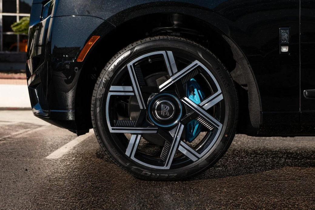 Close-up of a luxury car wheel with visible brand emblem on a road.