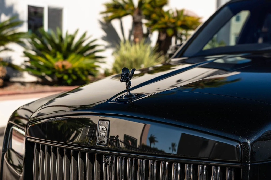 Close-up of a black Rolls-Royce car with palm trees in the background