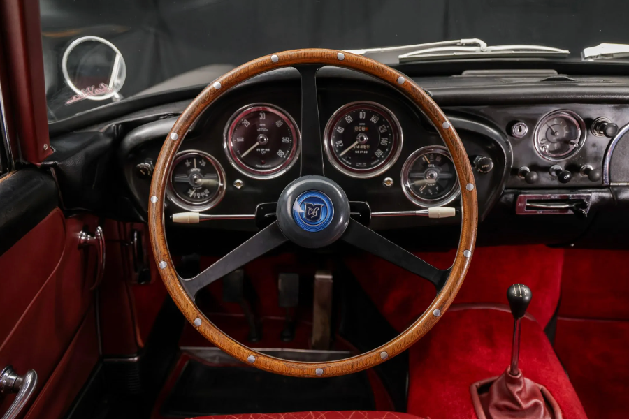 Close-up of a vintage car's steering wheel and dashboard with a visible brand logo.