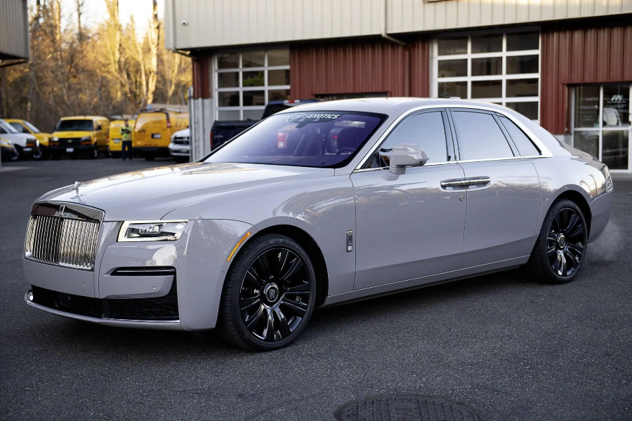 White Rolls-Royce Ghost parked in front of a building with other vehicles in the background.