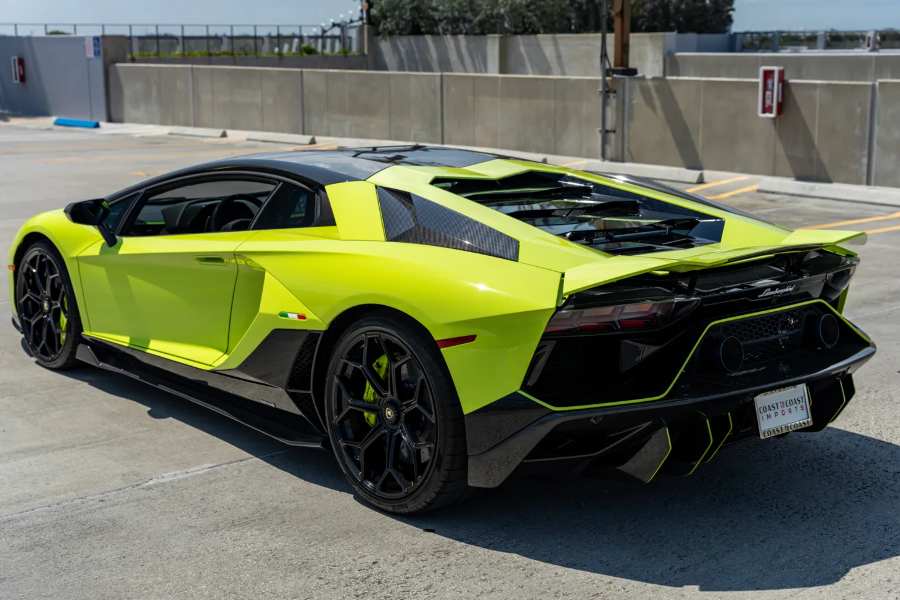 Lime green sports car parked on a concrete surface with a wall and trees in the background.