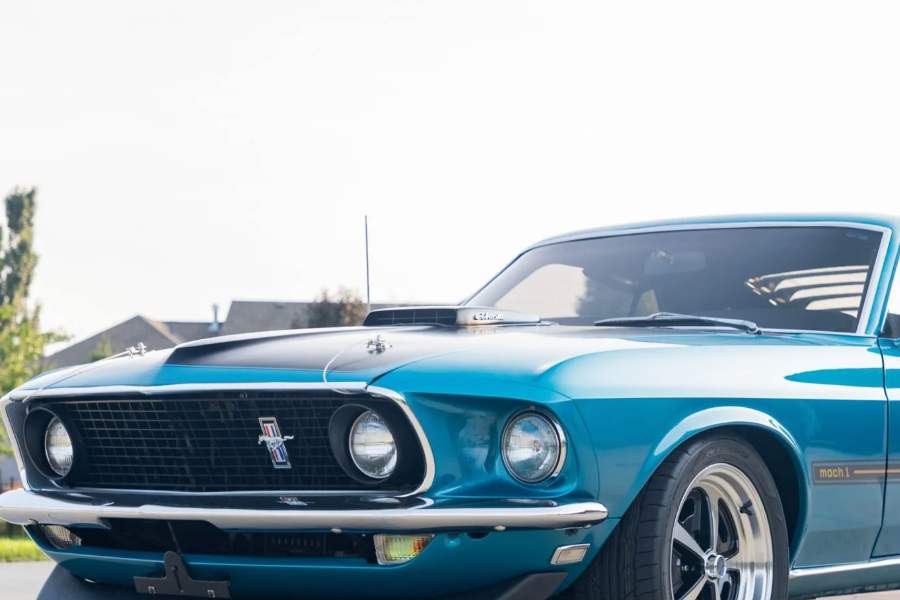 Blue Mustang car on a road with trees in the background