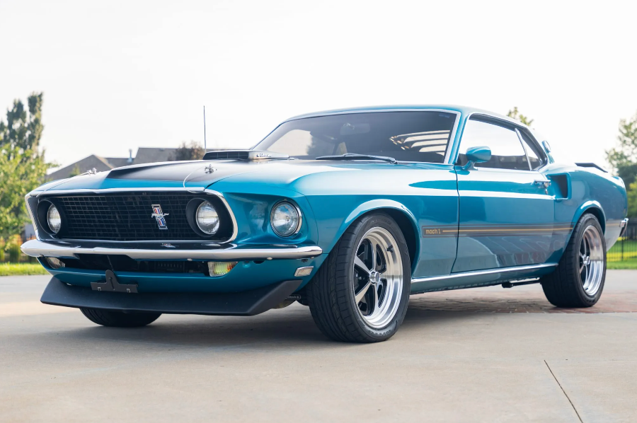 Blue classic Mustang parked on a street with trees in the background