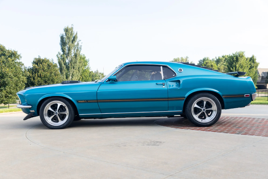Blue muscle car parked on a driveway with trees in the background
