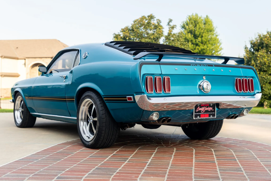 Blue muscle car parked on a brick driveway with trees in the background