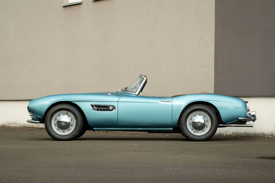 Vintage blue convertible car parked on a street with a plain wall background