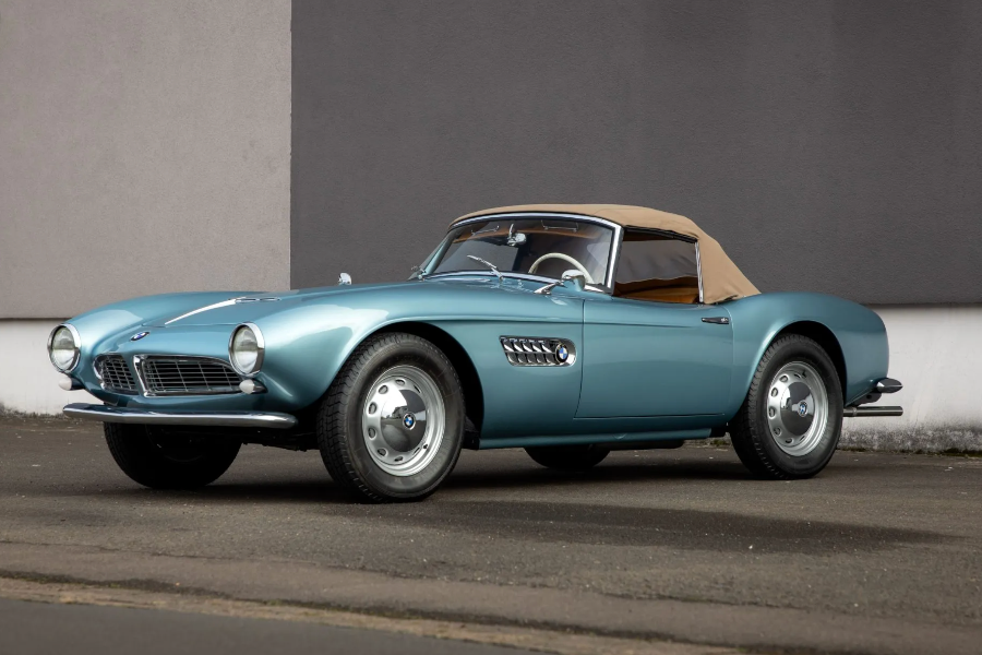 Vintage blue convertible car parked on a street with a gray wall in the background