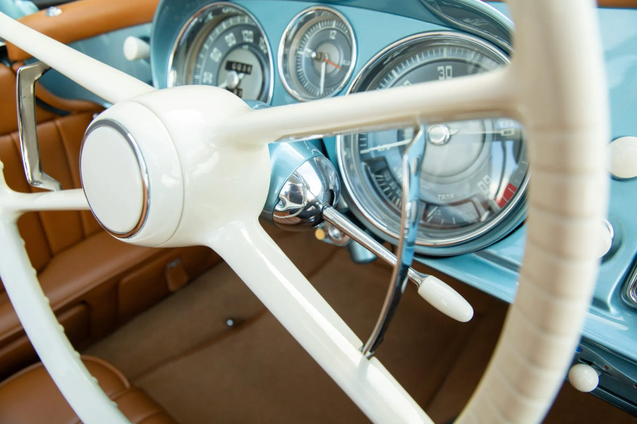 Close-up of a vintage car's steering wheel and dashboard with a white steering wheel and brown leather interior.