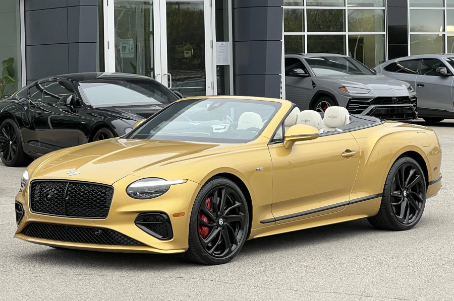 Gold Bentley convertible parked in front of a car dealership