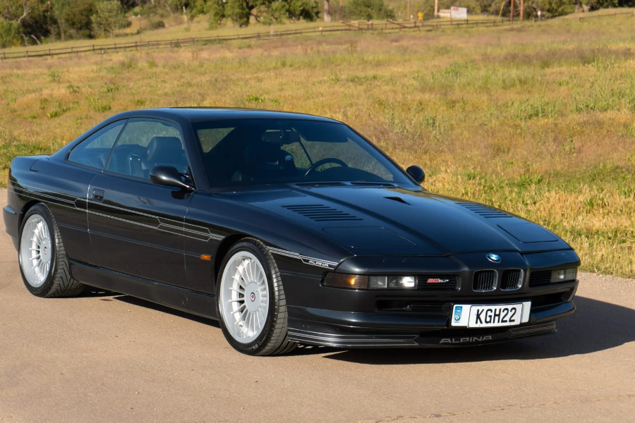 Black BMW Alpina car on a road with a grassy field in the background