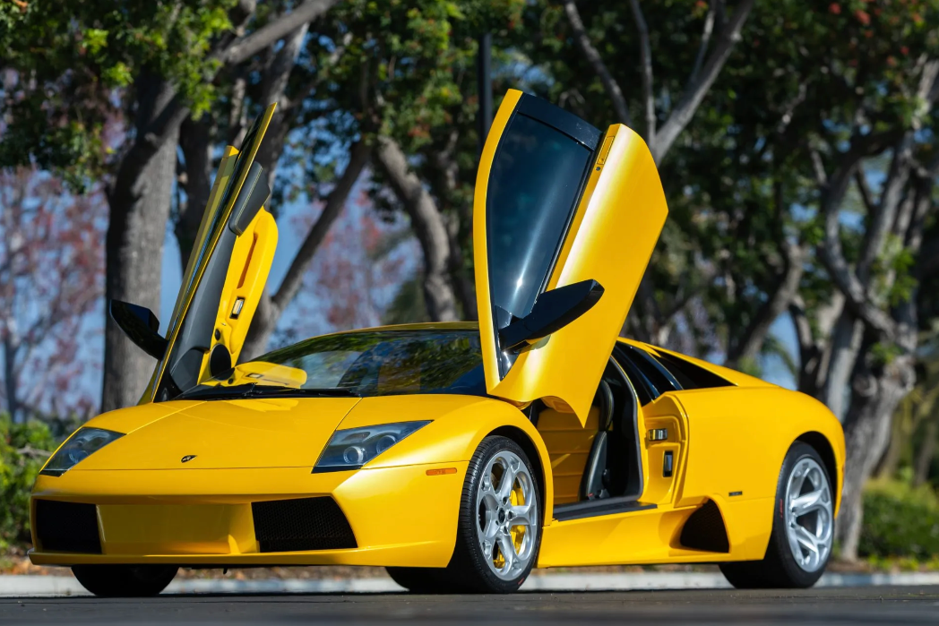 Yellow sports car with open doors on a road with trees in the background