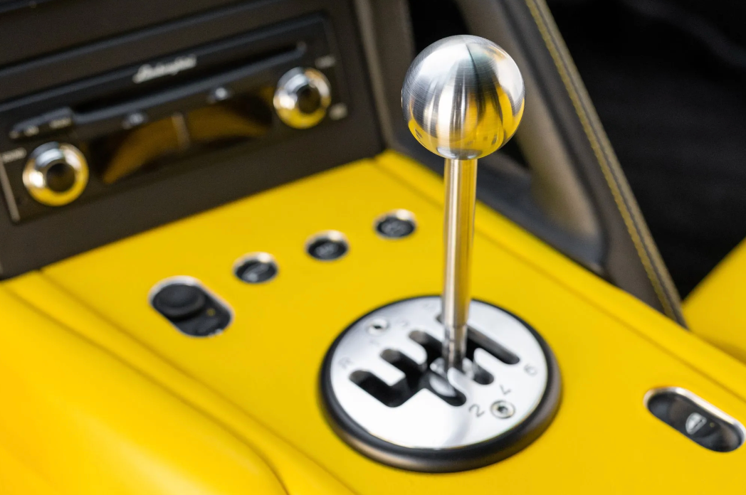 Close-up of a car's manual gear shift lever on a yellow dashboard.