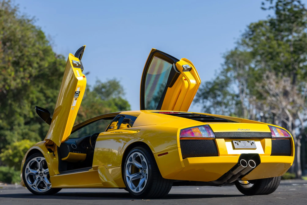 Yellow sports car with open doors on a road with trees in the background