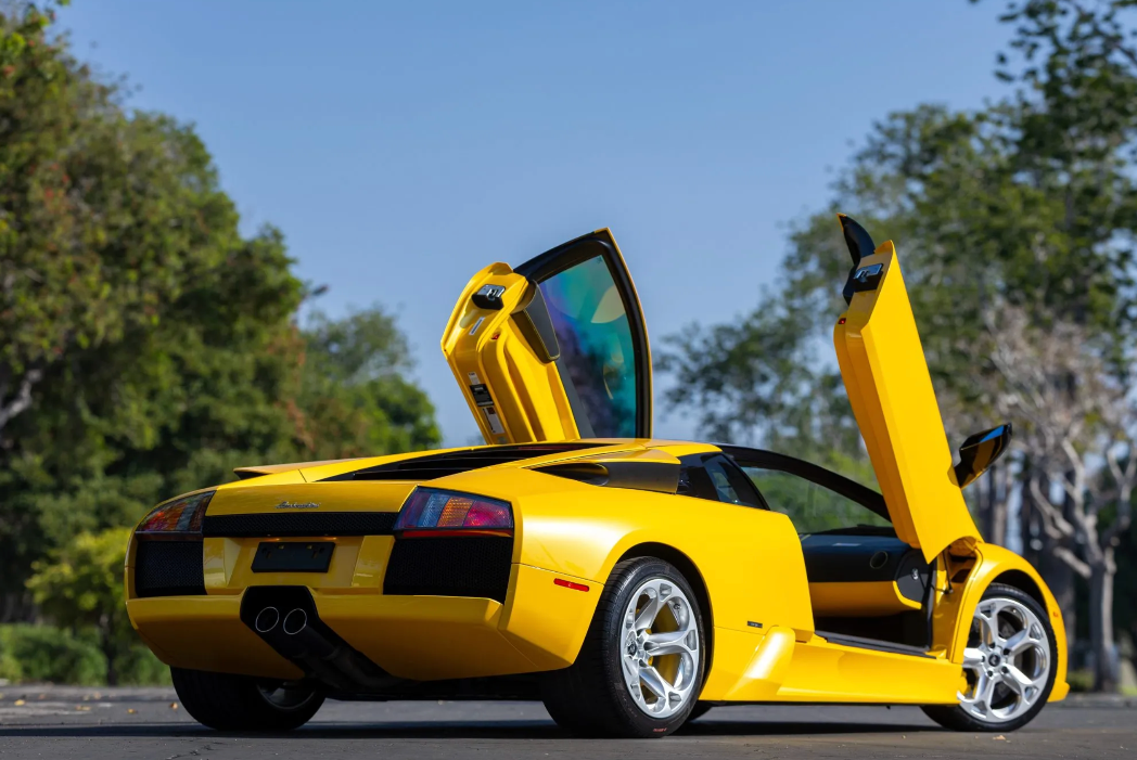 Yellow sports car with open doors on a road with trees in the background