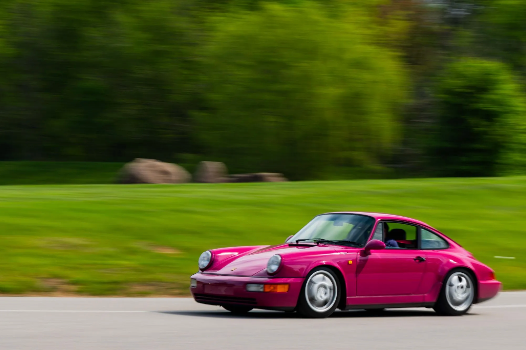 Pink sports car driving on a road with greenery in the background